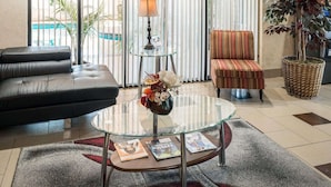 Ein Wohnzimmer mit einem Ledersofa, einem Glastisch mit Zeitschriften, einem gestreiften Sessel, einer Lampe und einer großen Topfpflanze.