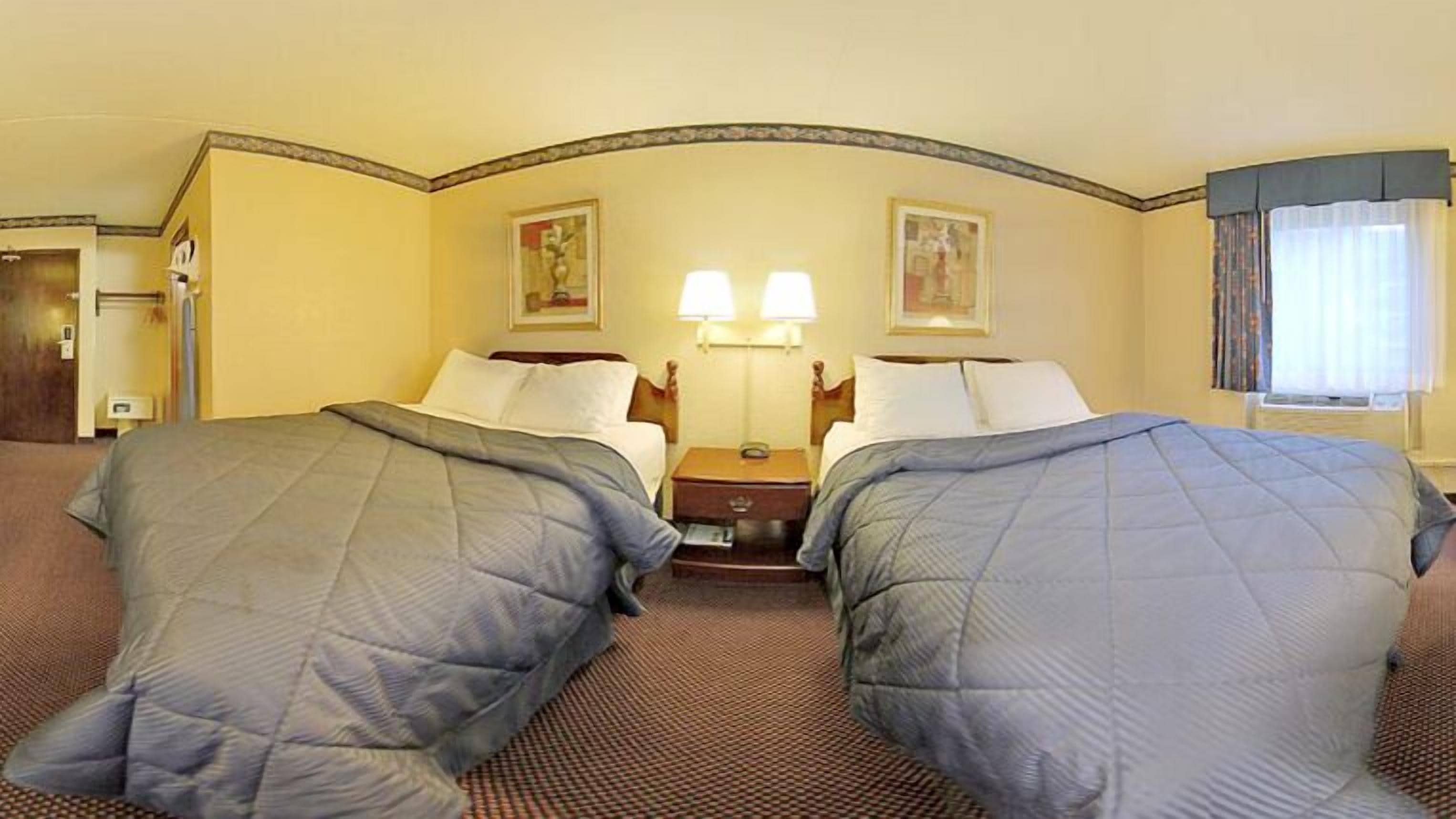A hotel room with two beds, a nightstand, two wall-mounted lamps, and a window with curtains.