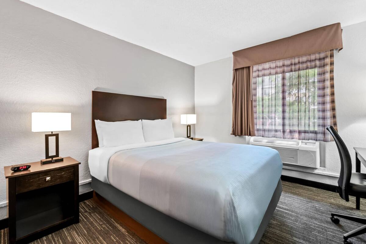 A hotel room with a large bed, two bedside tables with lamps, a desk, and a chair.