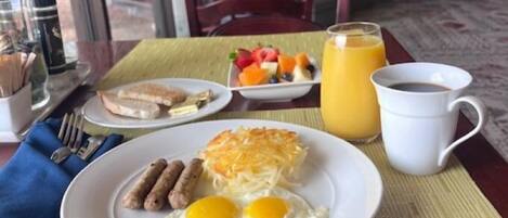 A breakfast table with eggs, sausages, hash browns, and a fruit bowl.