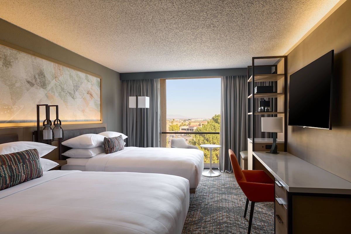 Une chambre d’hôtel avec deux lits, un bureau, une télévision et un balcon donnant sur la ville.