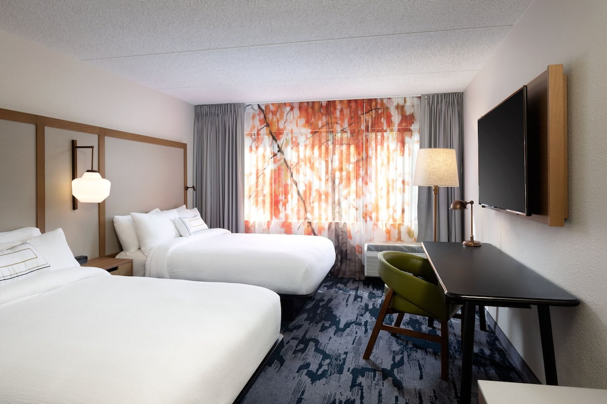 A hotel room with two beds, a desk, a chair, a TV, and a window with curtains.
