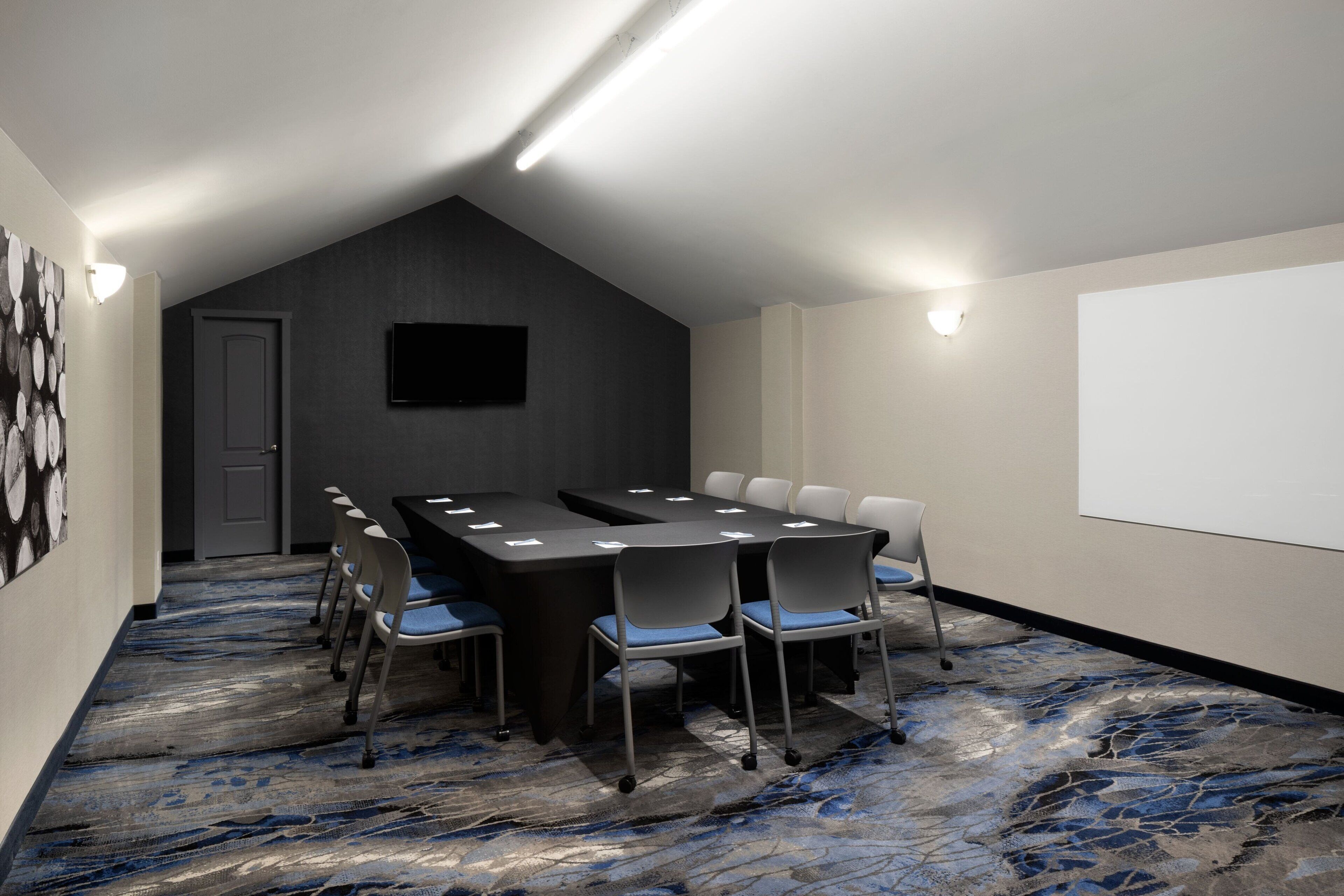 A conference room with a long table, chairs, a projector screen, and a carpeted floor.