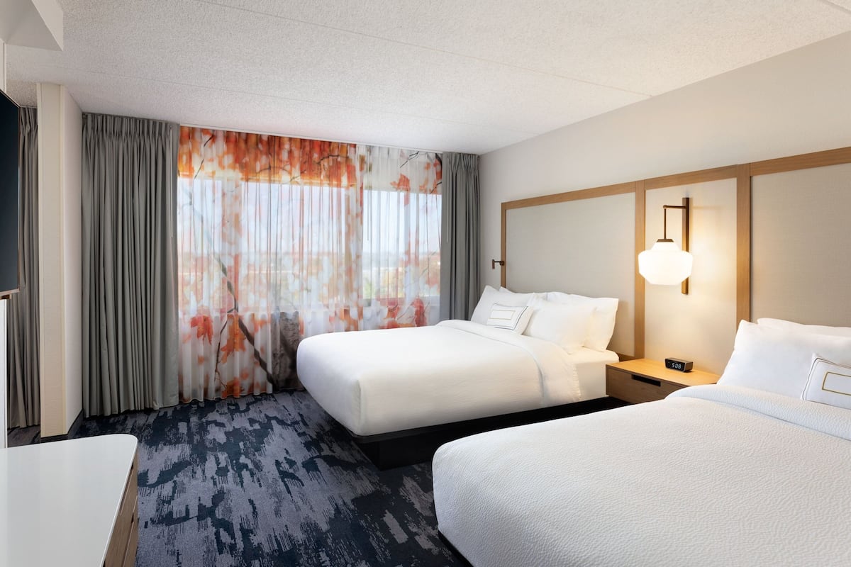 A hotel room with two beds, a desk, and a large window with curtains.