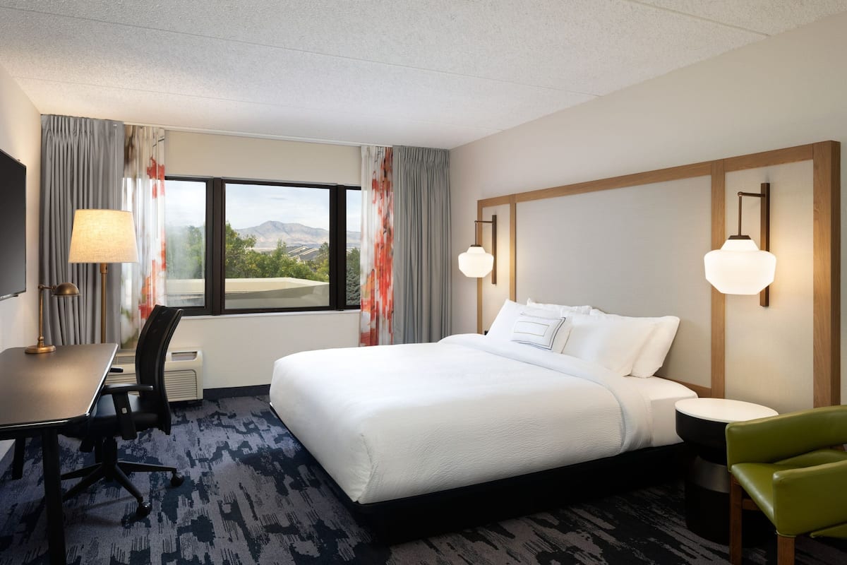 A hotel room with a large bed, a desk, a chair, and a view of the outdoors.