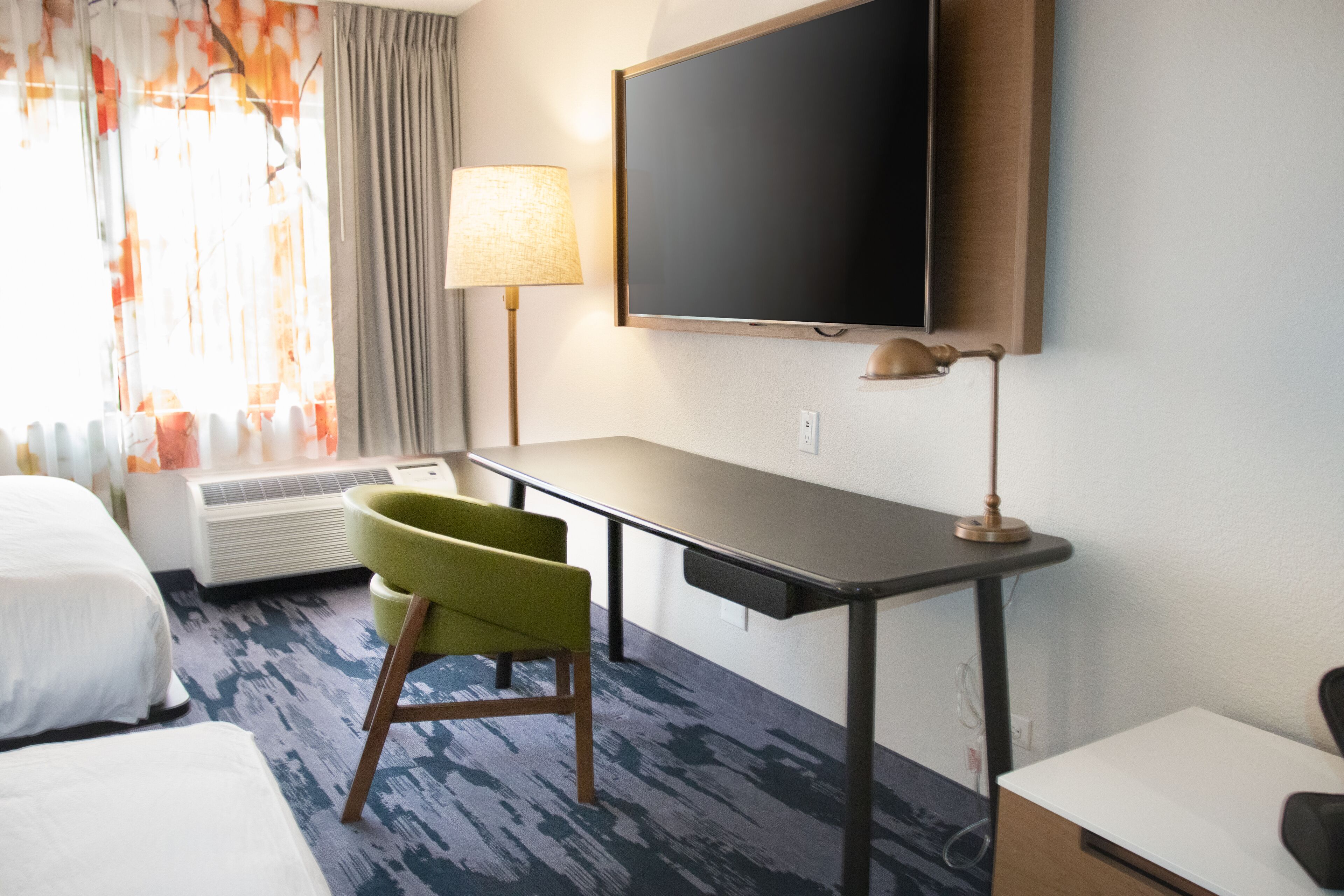 A hotel room with a bed, a desk, a chair, a TV, and a window with curtains.