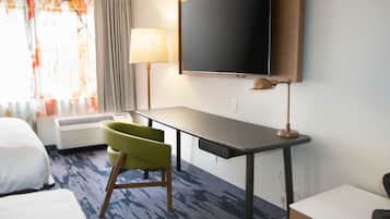 A hotel room with a bed, a desk, a chair, a TV, and a window with curtains.