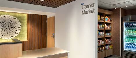 A modern interior with a reception desk, a large decorative wall piece, and shelves stocked with snacks and beverages.