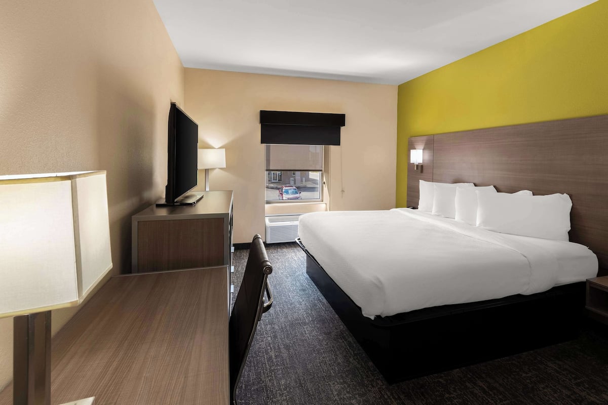 A hotel room with a bed, a desk with a lamp, a television, and a window with a view of the outside.