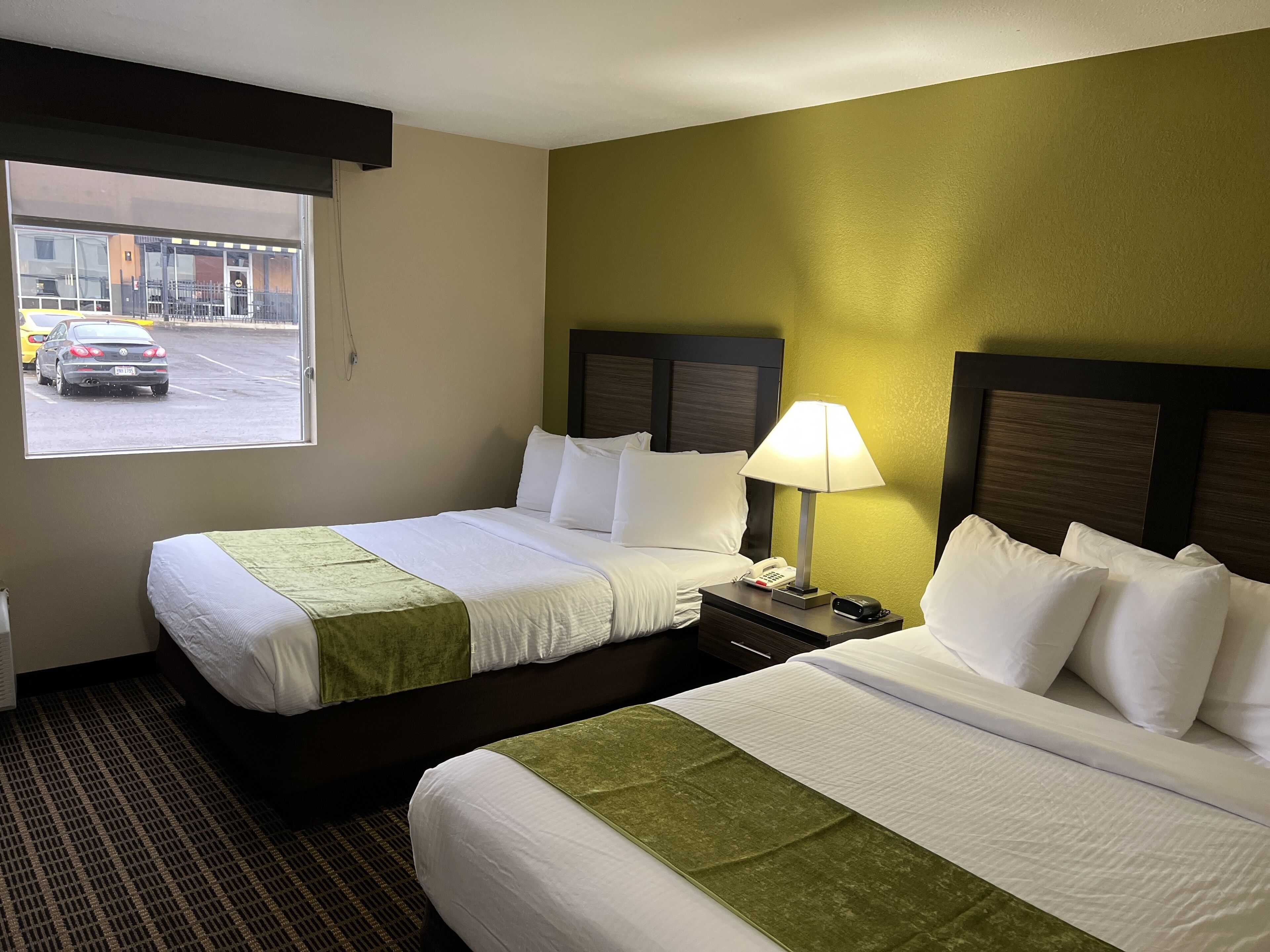 A hotel room with two beds, a window with a view of the street, a lamp, and a telephone on the nightstand.