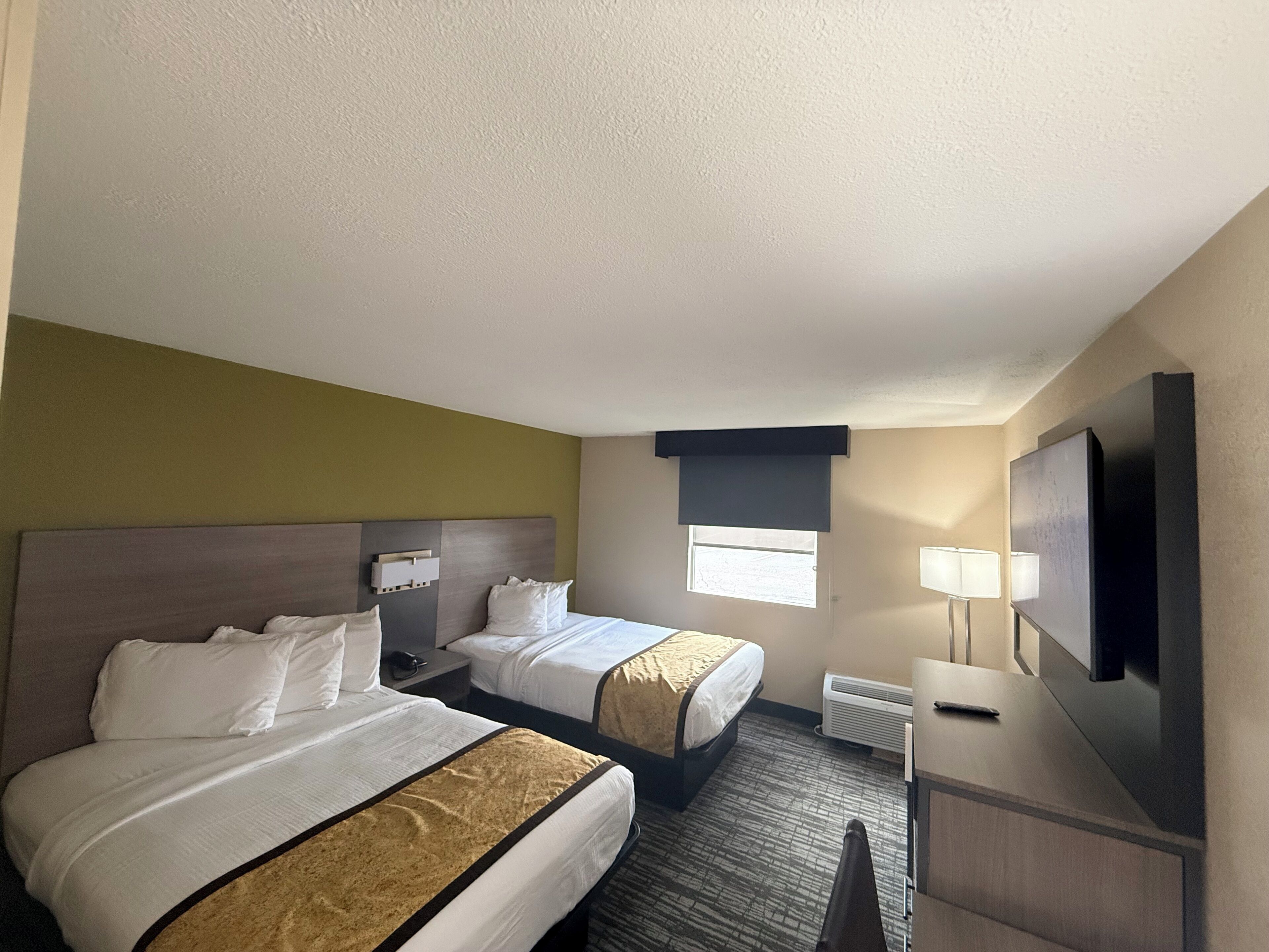 A hotel room with two beds, a desk, a TV, and a window.