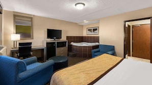 A hotel room with a bed, two armchairs, a desk with a computer, a TV, a hot tub, and a wooden door. - Best Western Adena Inn (Chillicothe)