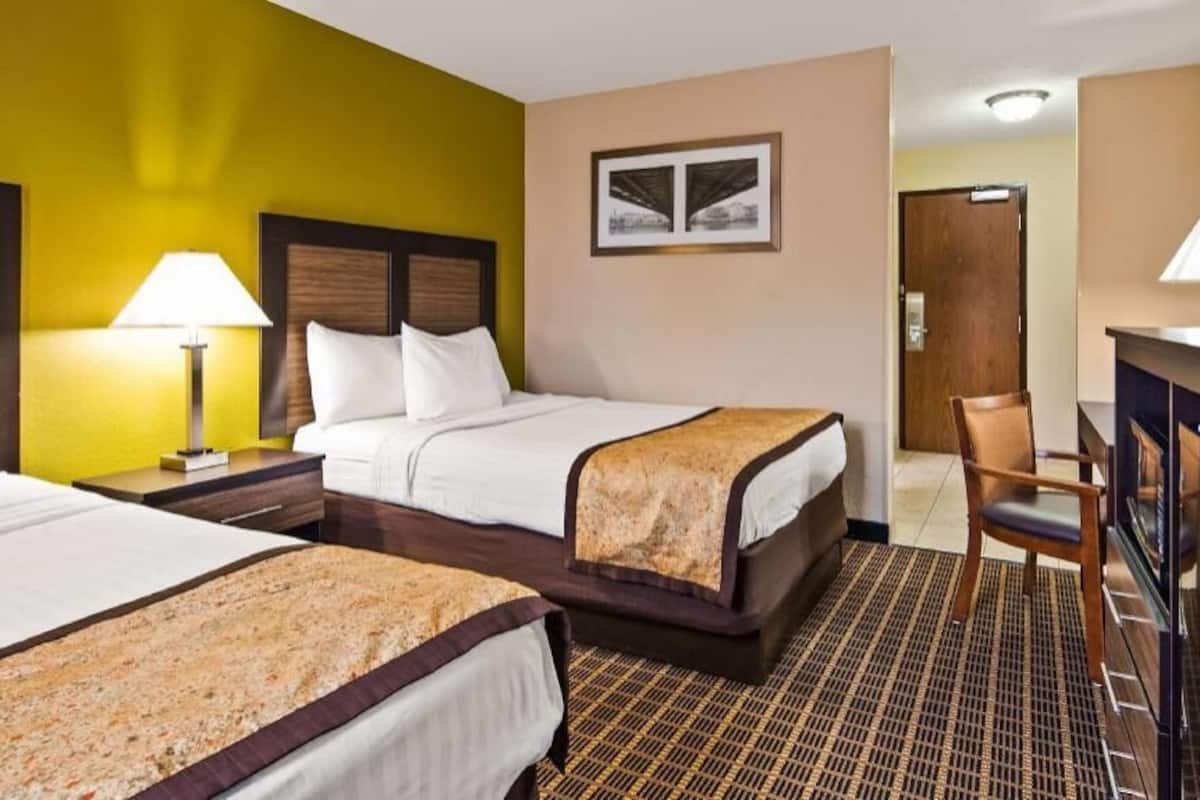 A hotel room with two beds, a desk with a TV, and a chair.