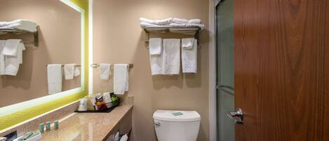 Et badeværelse med vask, toilet og et spejl med gul ramme. Der er håndklæder på væggen og en trædør.