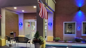 A building entrance with a brick facade, American flag, blue lights, a wheelchair parking sign, and outdoor seating. - Best Western Adena Inn (Chillicothe)