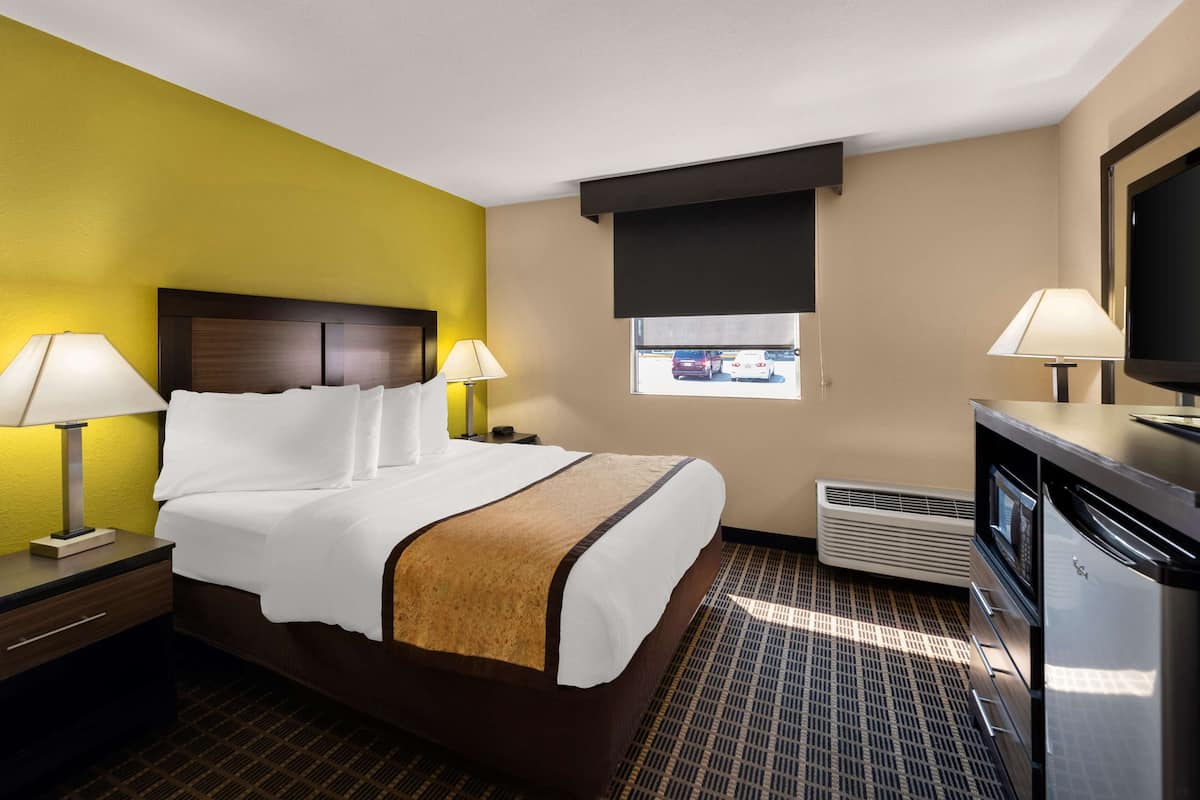 A hotel room with a bed, two bedside tables with lamps, a window, a television, and a kitchenette.