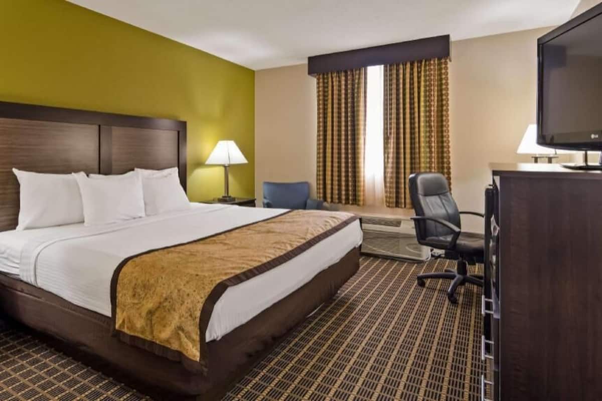 A hotel room with a large bed, two bedside tables, a desk with a chair, a television, and a window with curtains.
