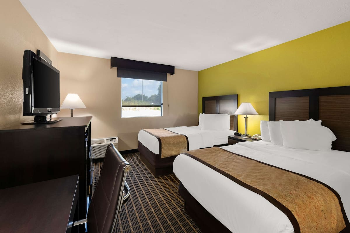 A hotel room with two beds, a desk with a TV, and a window with a view.