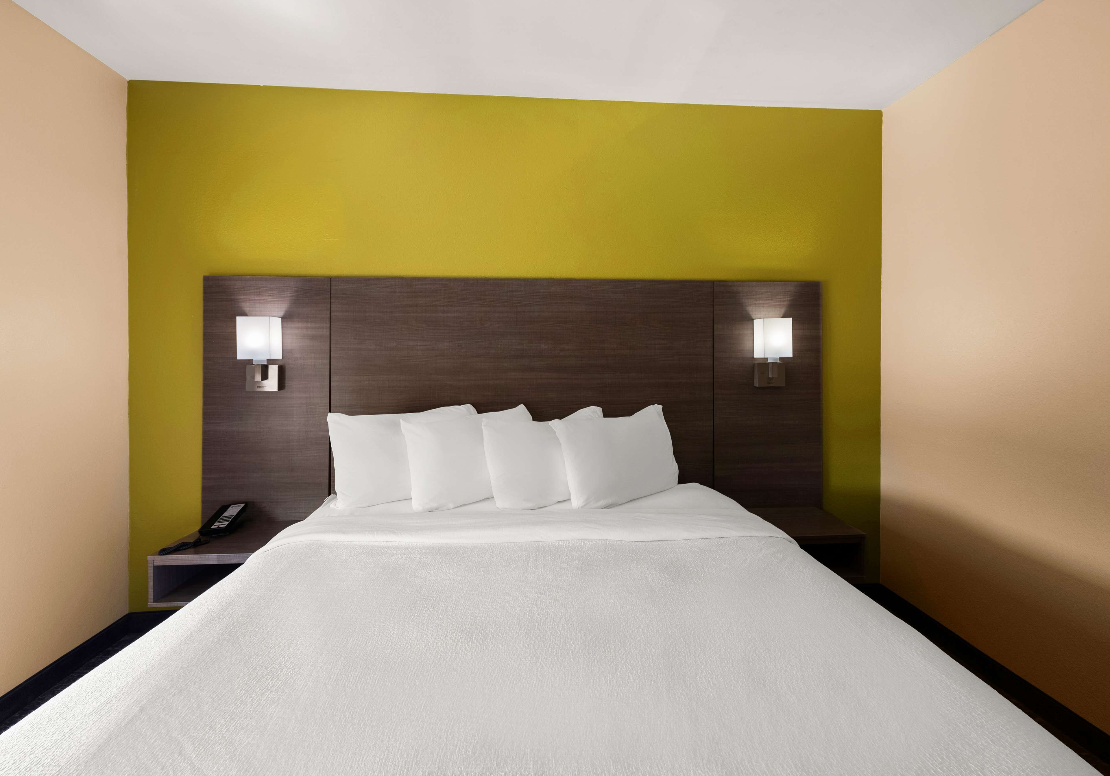 Habitación de hotel con una cama grande, dos mesitas de noche y una mesita con un teléfono.