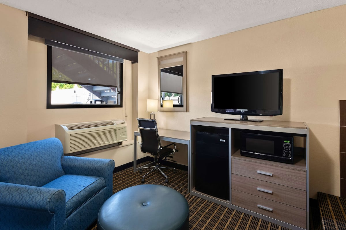 A hotel room with a blue sofa, a desk with a chair, a television, a microwave, and a minibar.