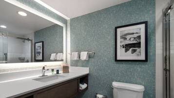 A modern bathroom with a large mirror, white sink, and a framed picture on the wall.