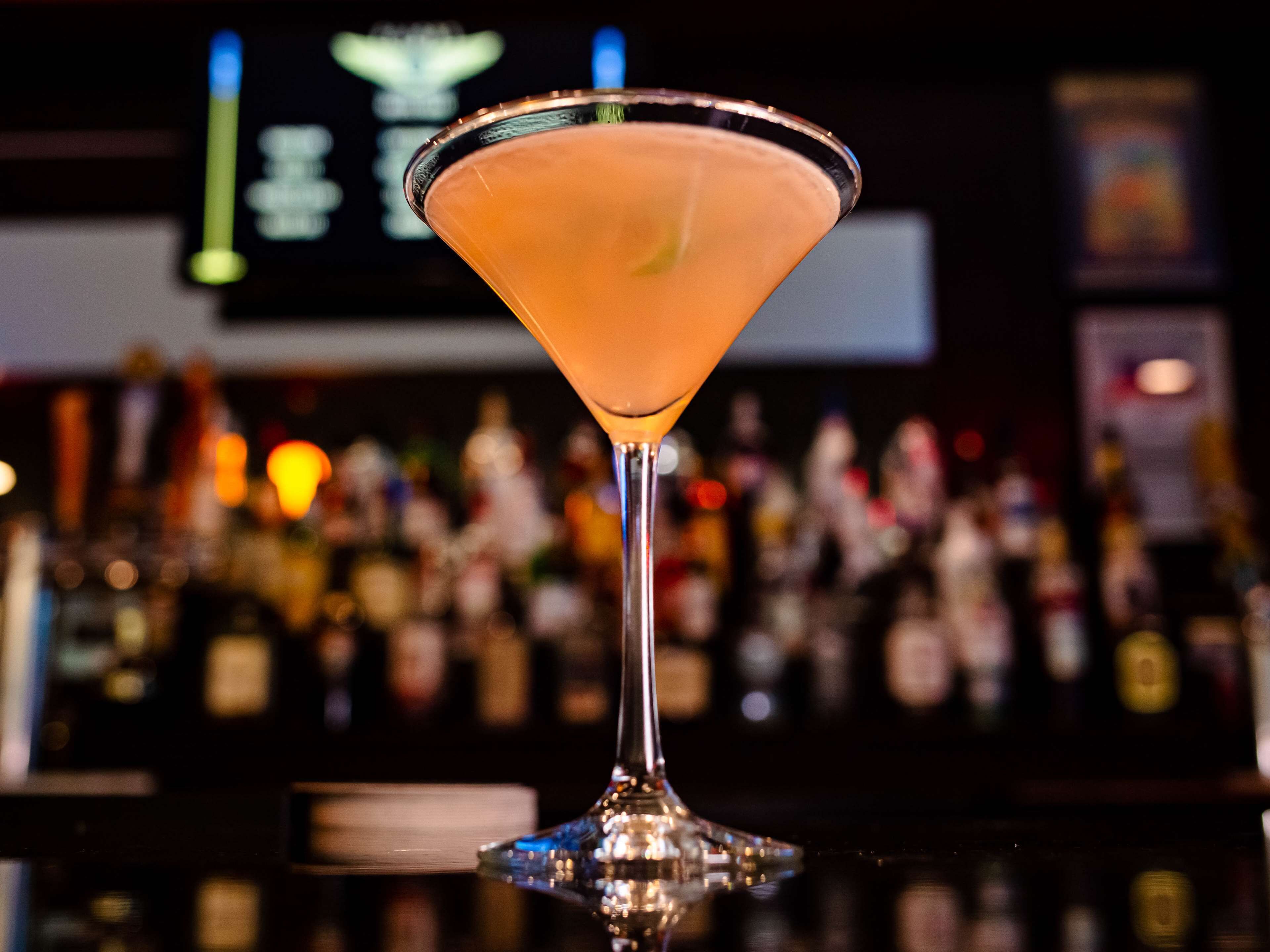 A martini glass on a bar counter with a blurred background of bottles.
