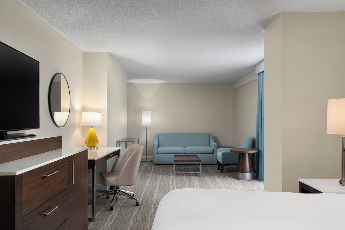 Ein Hotelzimmer mit Bett, Schreibtisch mit Stuhl, Sofa, Fernseher und Lampe.