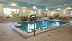 Un espace piscine offrant une vue dégagée sur l’extérieur, une piscine avec un escalier en métal, ainsi que plusieurs chaises et tables disposées autour.