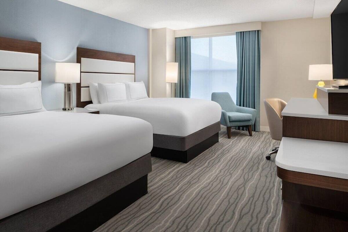 Quarto de hotel com duas camas, uma escrivaninha, uma cadeira e uma televisão.