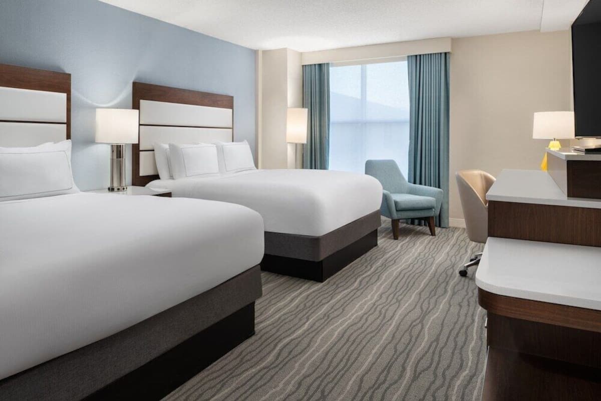 Quarto de hotel com duas camas, uma escrivaninha, uma cadeira e uma televisão.