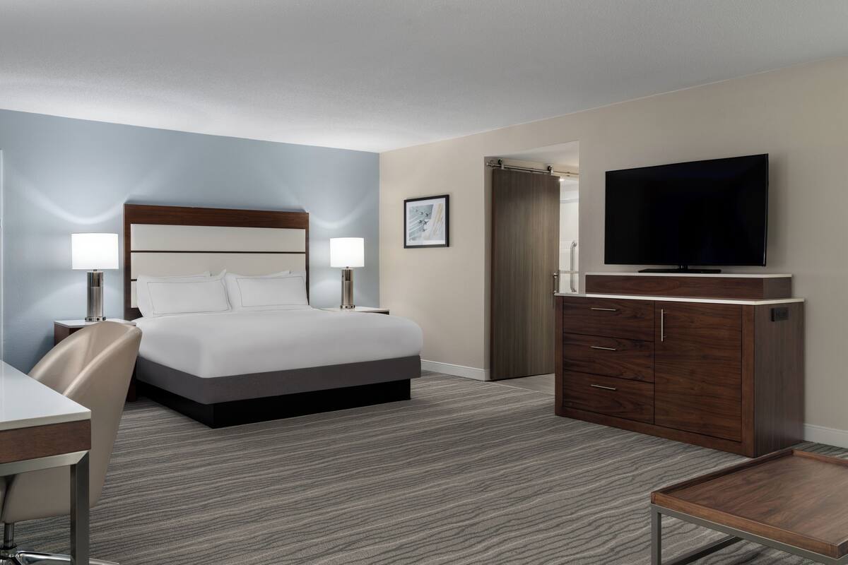 Ein Hotelzimmer mit Bett, Nachttischlampen, Fernseher, Schreibtisch und Stuhl.