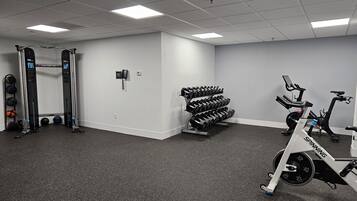 A gym with a squat rack, dumbbells, an exercise bike, and a wall-mounted phone.