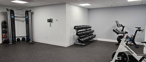 Ein Fitnessstudio mit Squat-Rack, Kurzhanteln, einem Ergometer und einem an der Wand montierten Telefon.