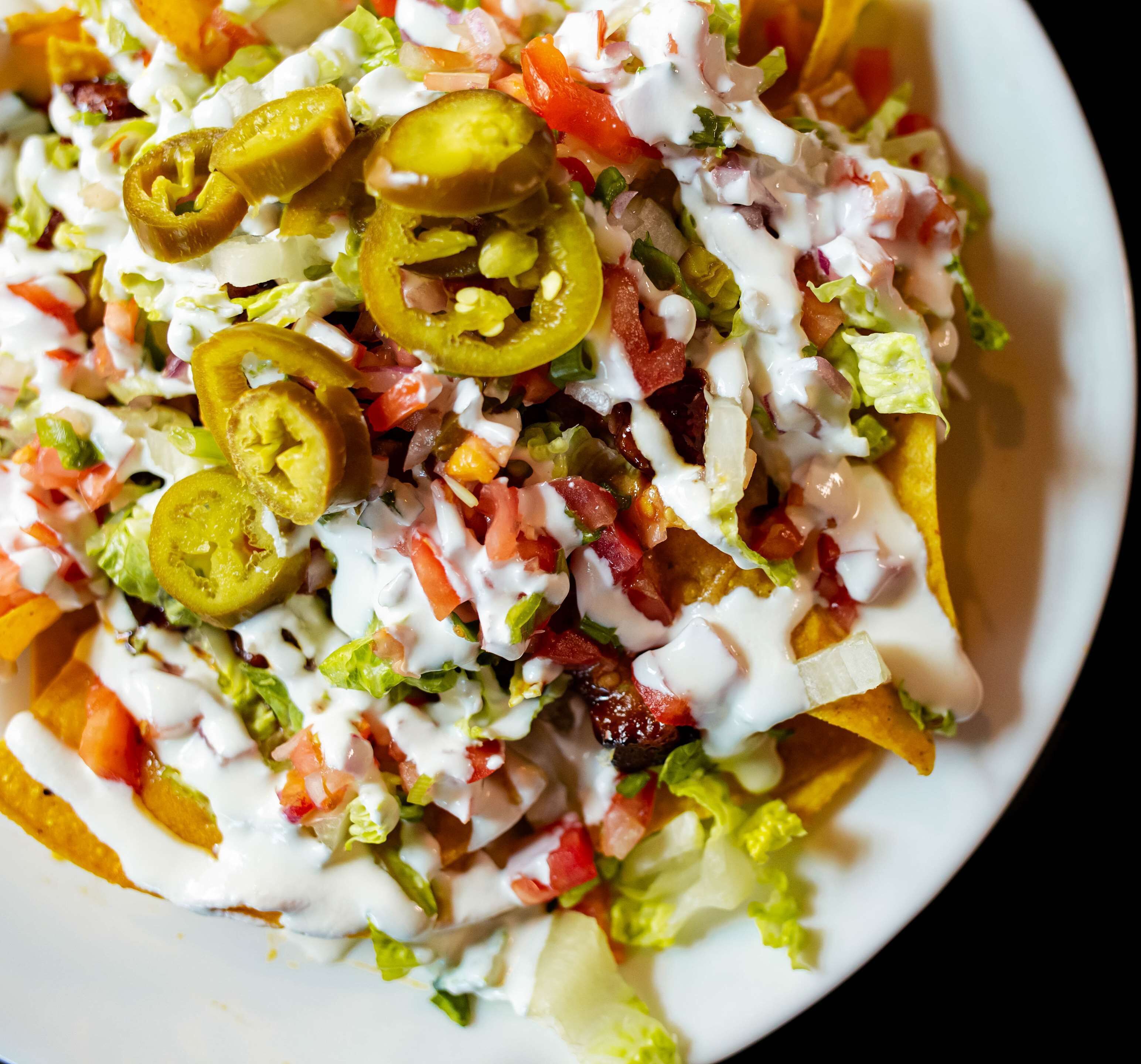 Nachos cubiertos de jalapeños, tomates, lechuga y salsa cremosa.