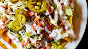 Nachos cubiertos de jalapeños, tomates, lechuga y salsa cremosa.