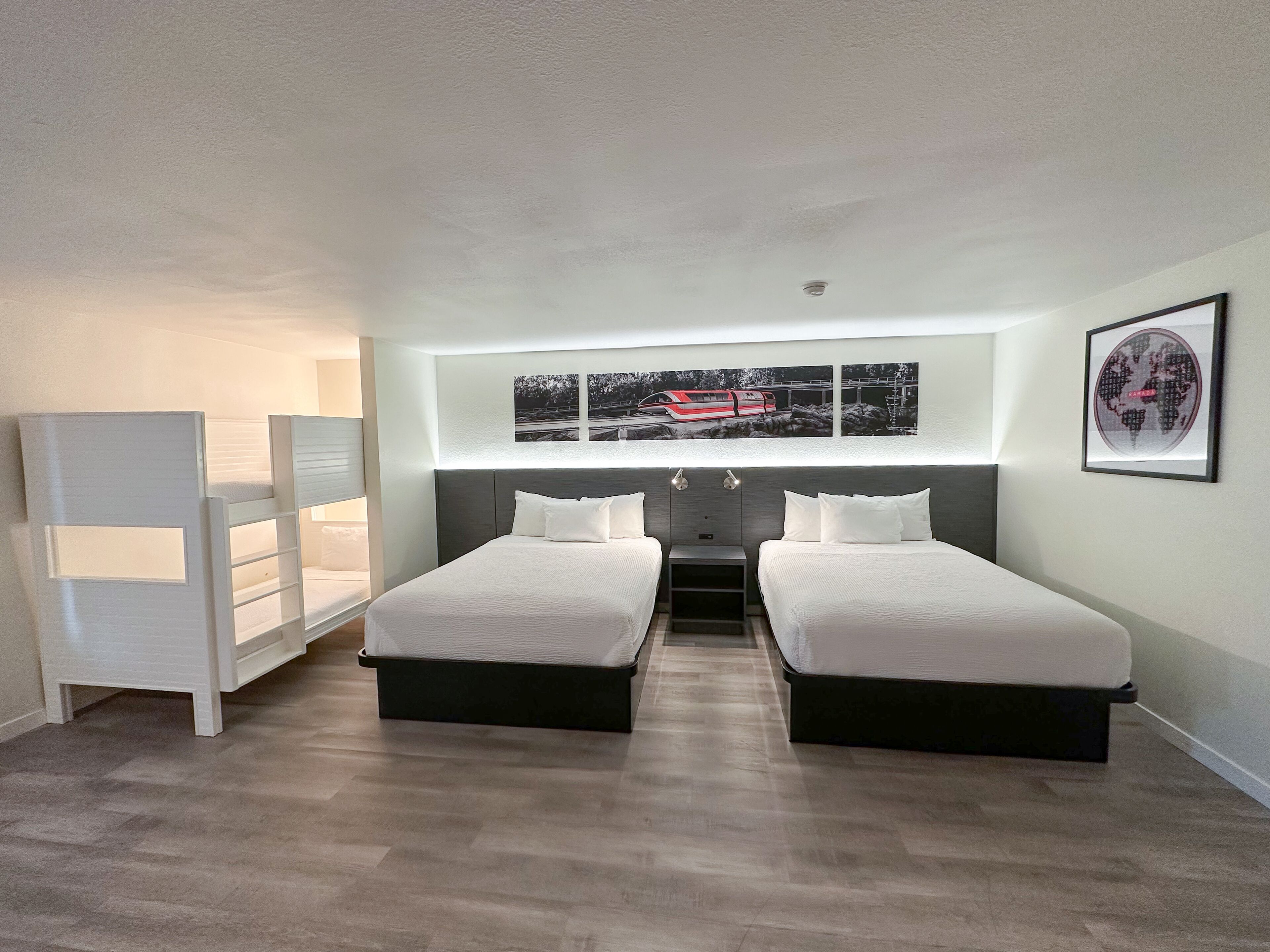 A modern bedroom with two beds, a white wardrobe, and a large window with artwork above.