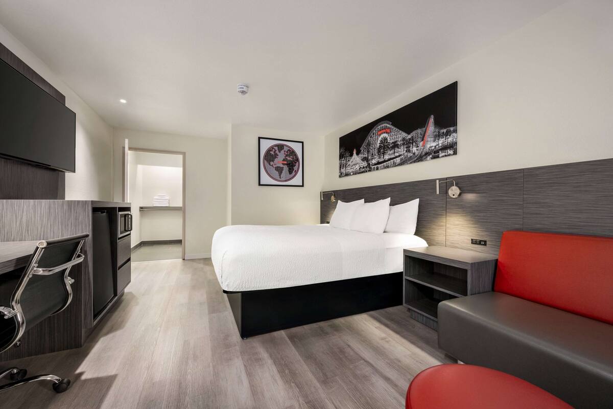 A hotel room with a bed, a desk, a red sofa, a TV, and a framed picture on the wall.