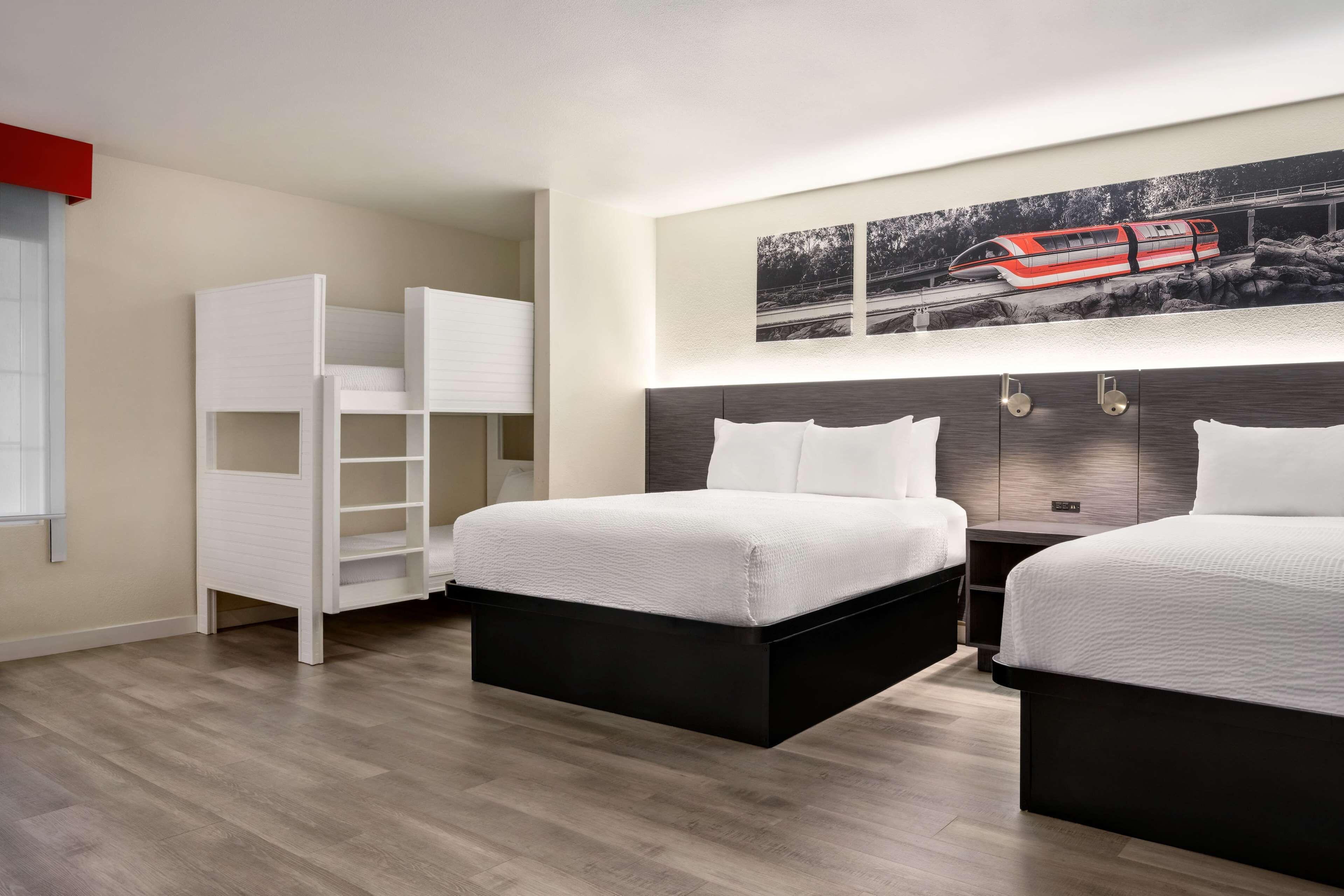 Habitación de hotel con dos camas, un armario blanco, un escritorio y un ventanal grande.