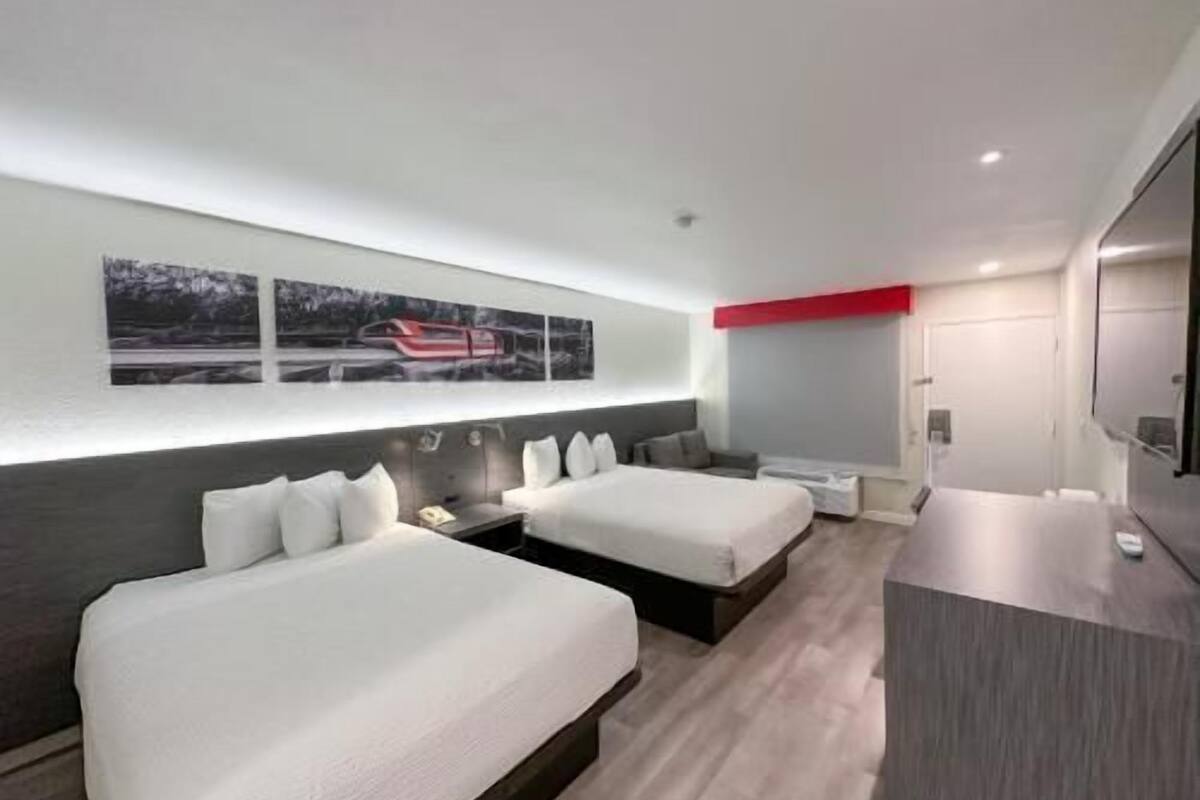 A modern hotel room with two beds, a desk, and a large window.