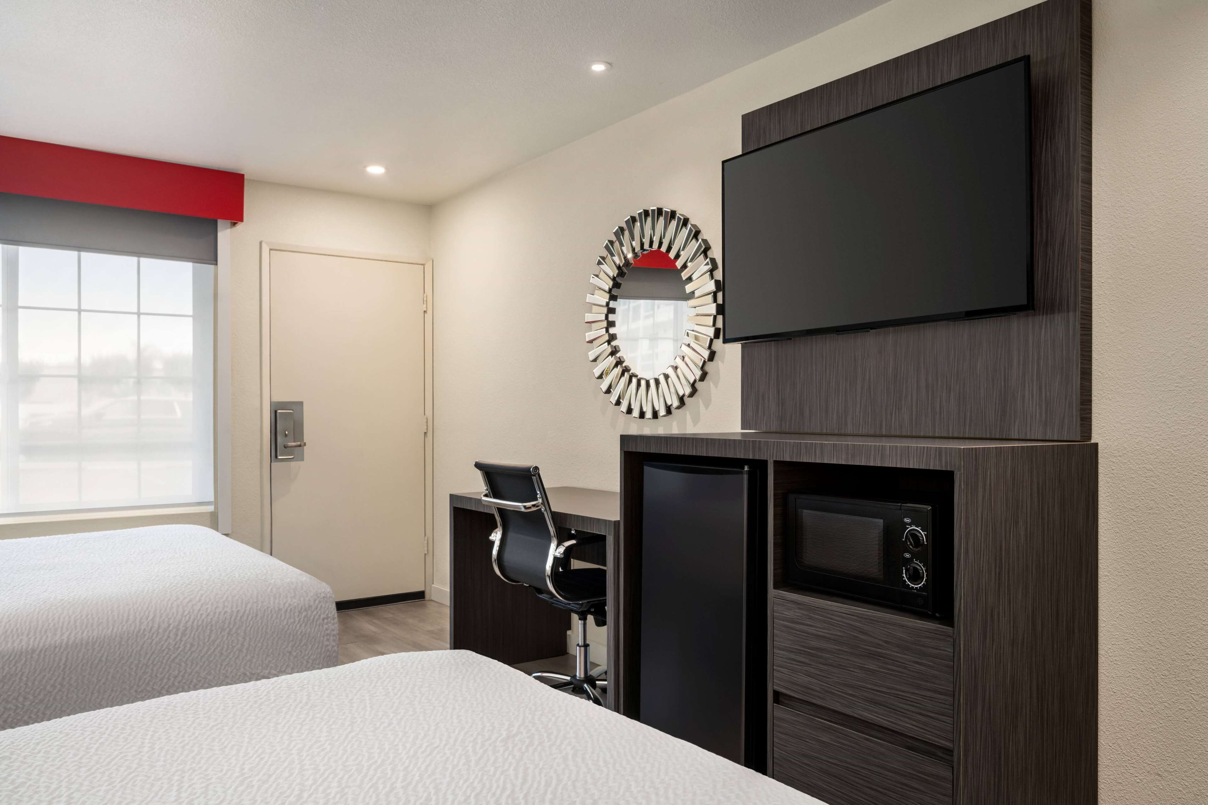 Habitación de hotel con dos camas, un escritorio con silla, televisión, microondas y un ventanal grande.