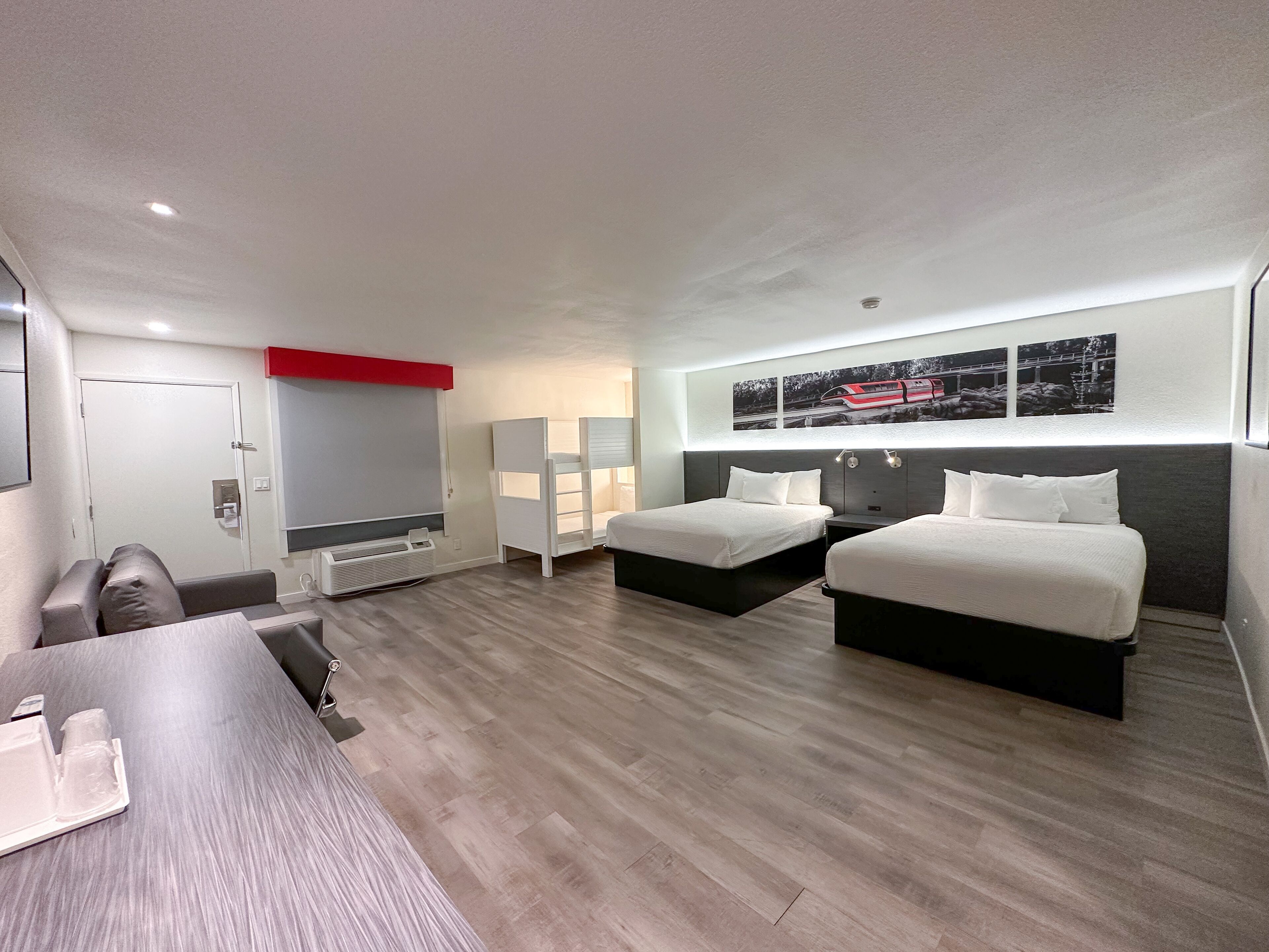 A modern hotel room with two beds, a desk, and a seating area.