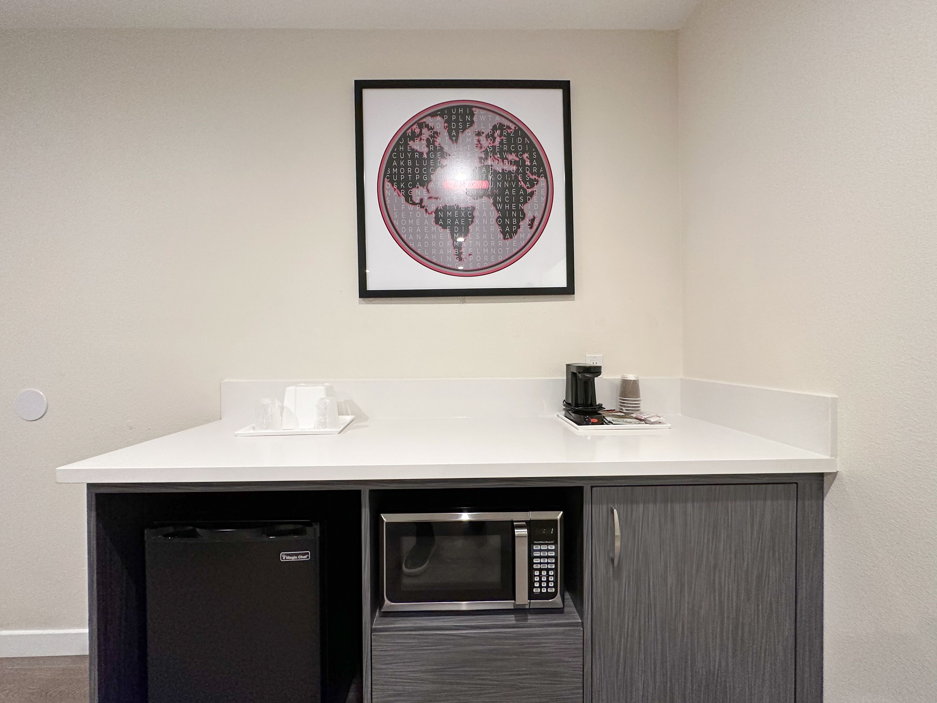 A kitchenette with a microwave, coffee maker, and a framed picture on the wall.