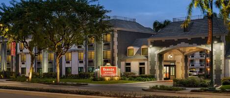 A multi-story hotel with a modern architectural design, featuring a prominent entrance with a sign, and a landscaped front yard.