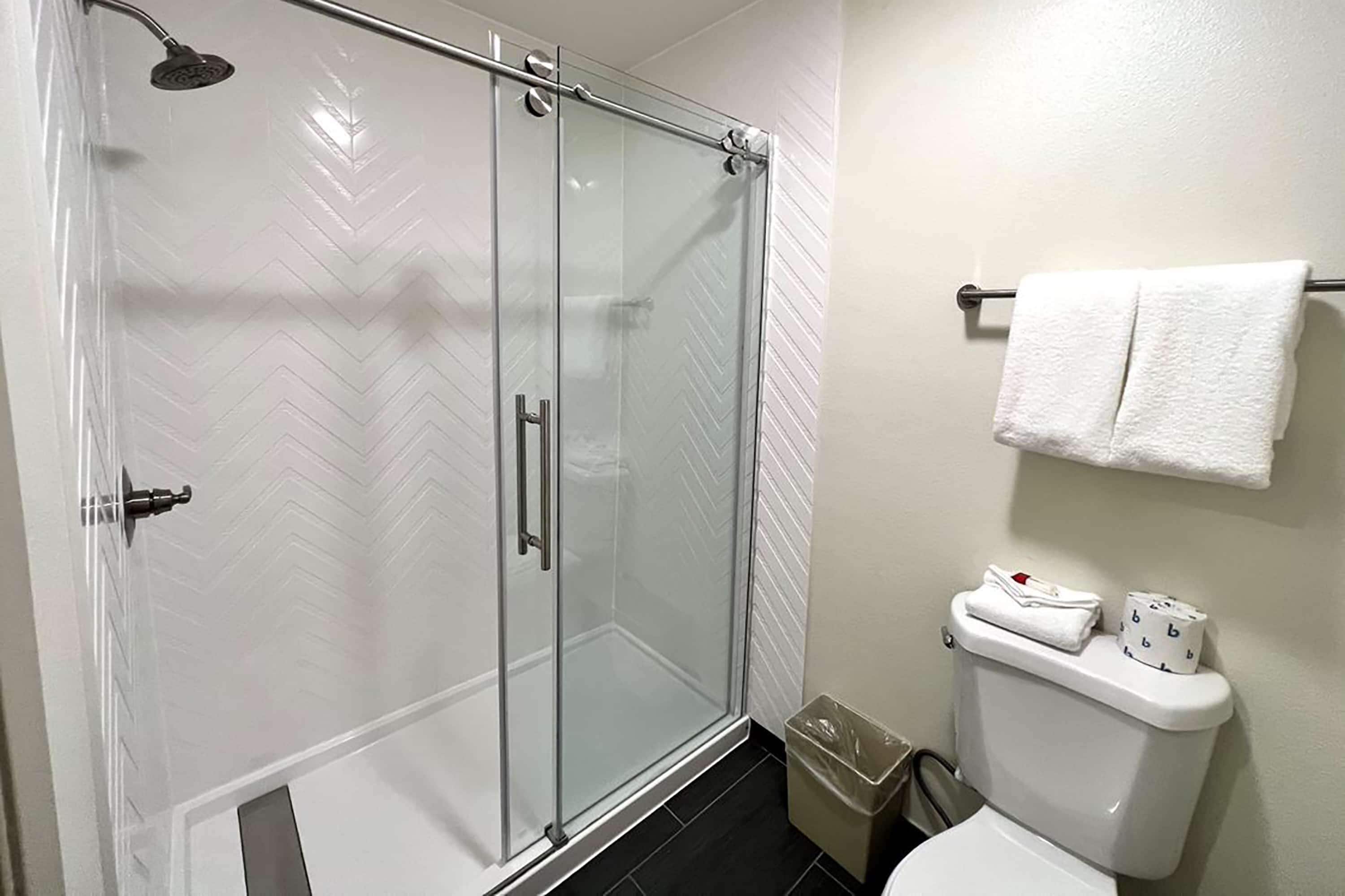 A bathroom with a glass-enclosed shower, a toilet with a white towel and toilet paper, and a trash bin.