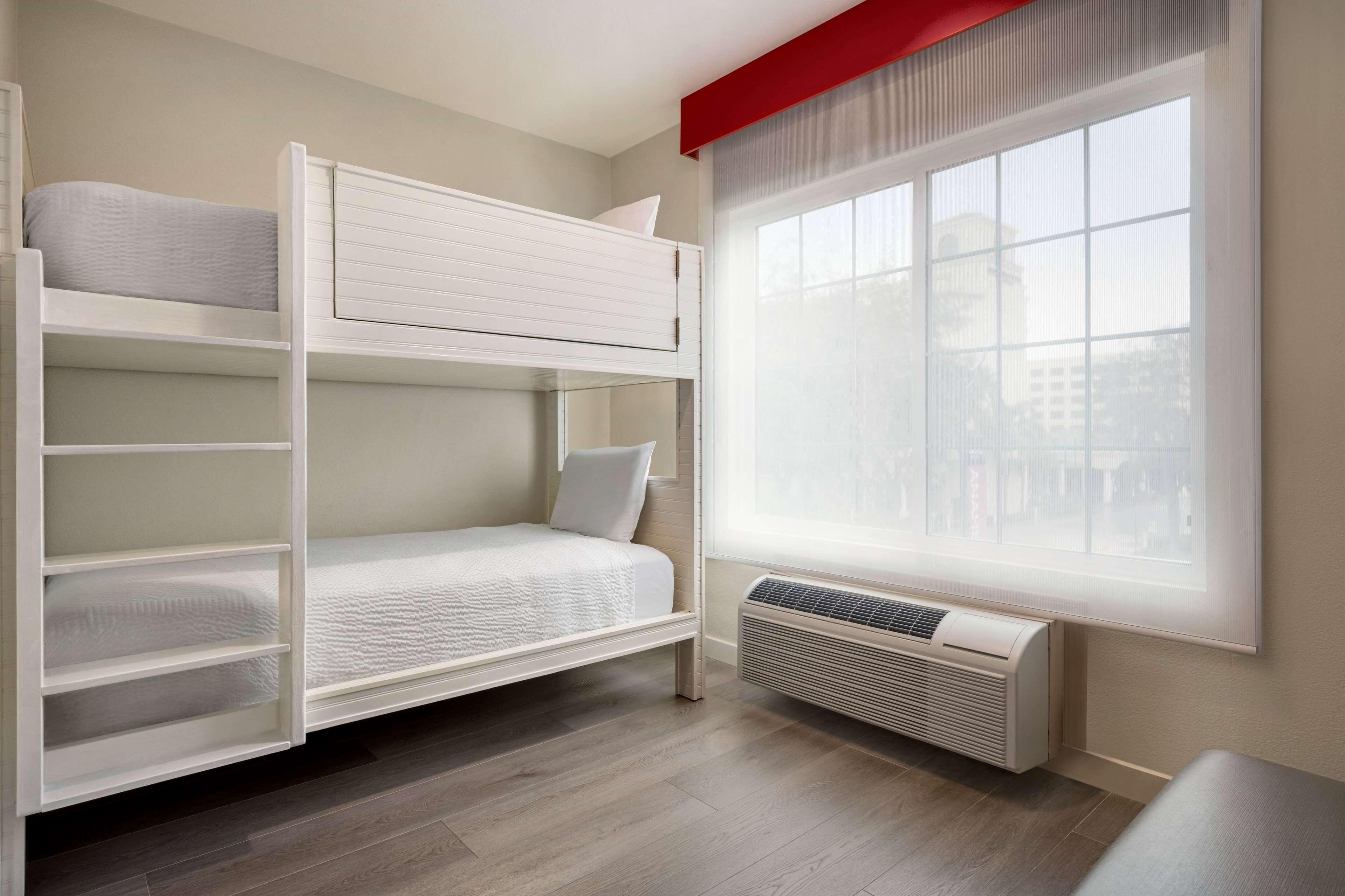 Une chambre avec un lit superposé, une fenêtre et un appareil de climatisation.