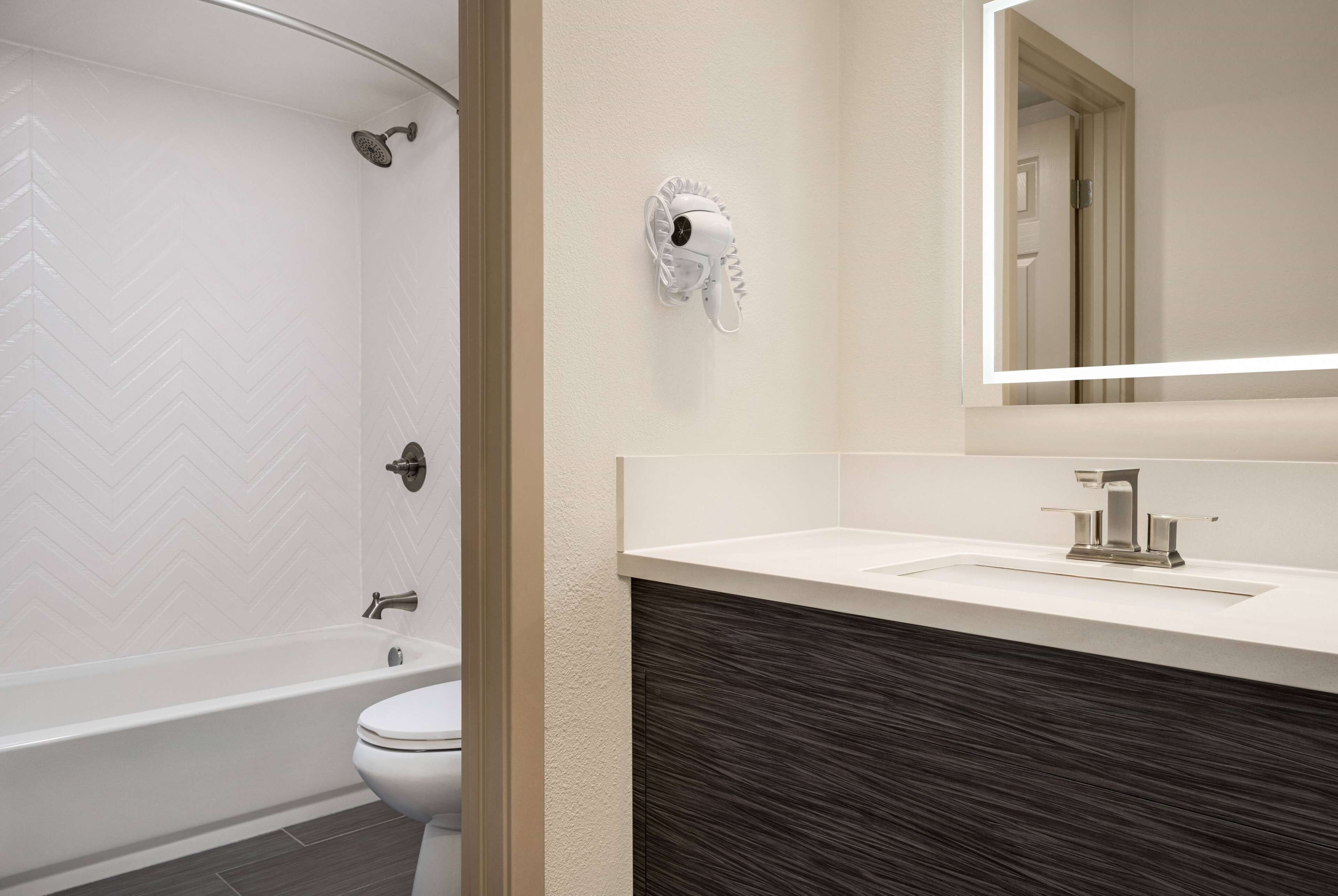 A modern bathroom with a freestanding bathtub, a toilet, and a vanity with a dark wood countertop.