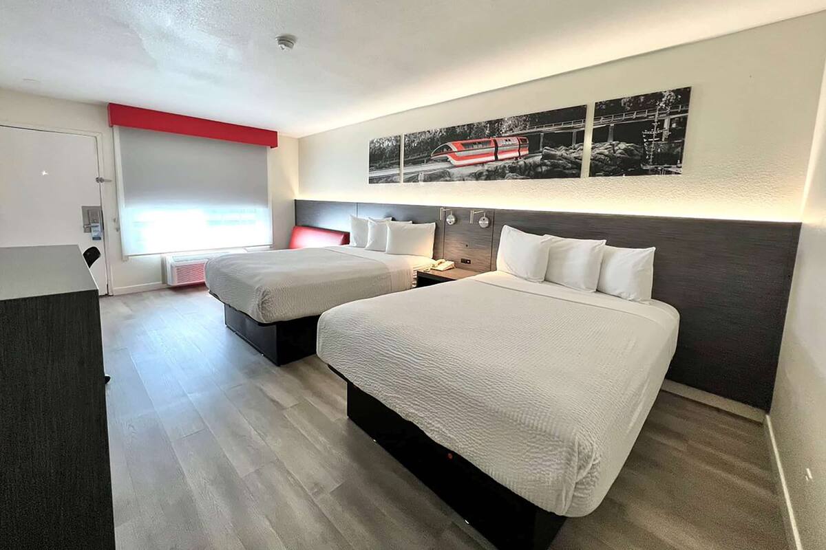 A hotel room with two beds, a red accent wall, and a large black-and-white photo above the beds.