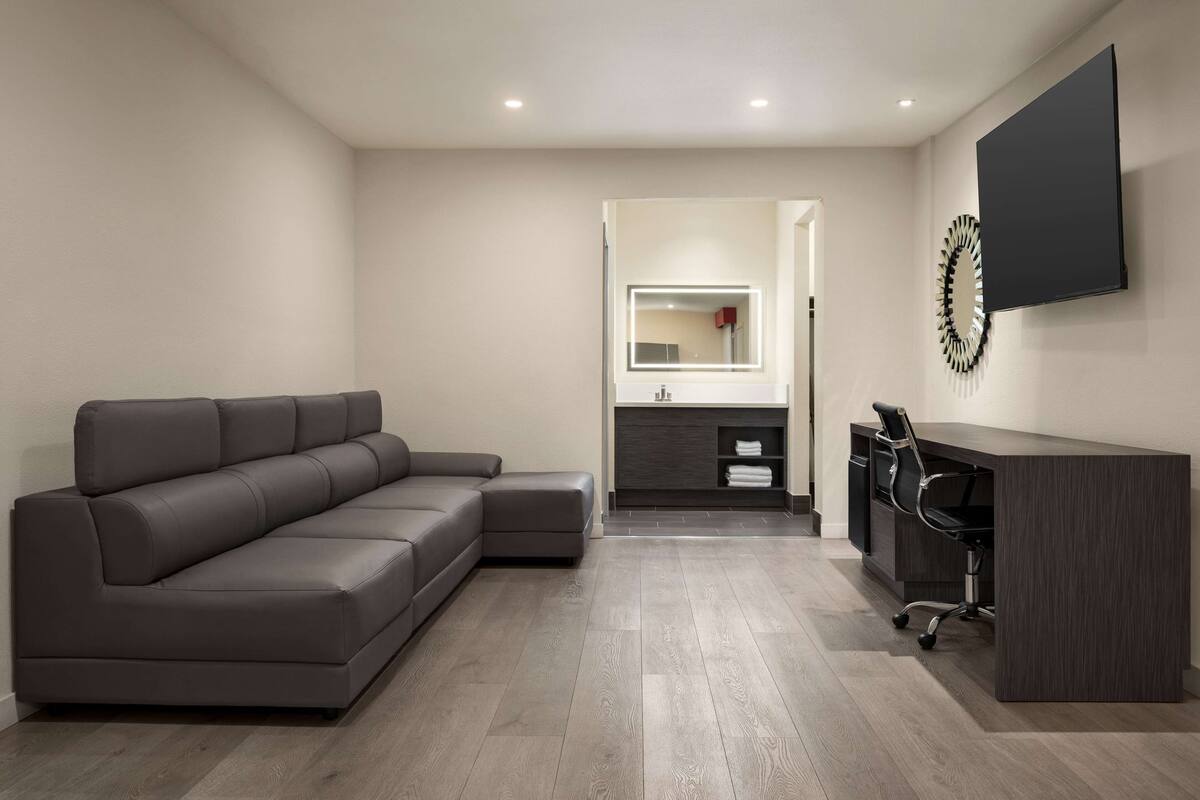 A modern living room with a sectional sofa, a dark wooden desk, and a large flat-screen TV mounted on the wall.