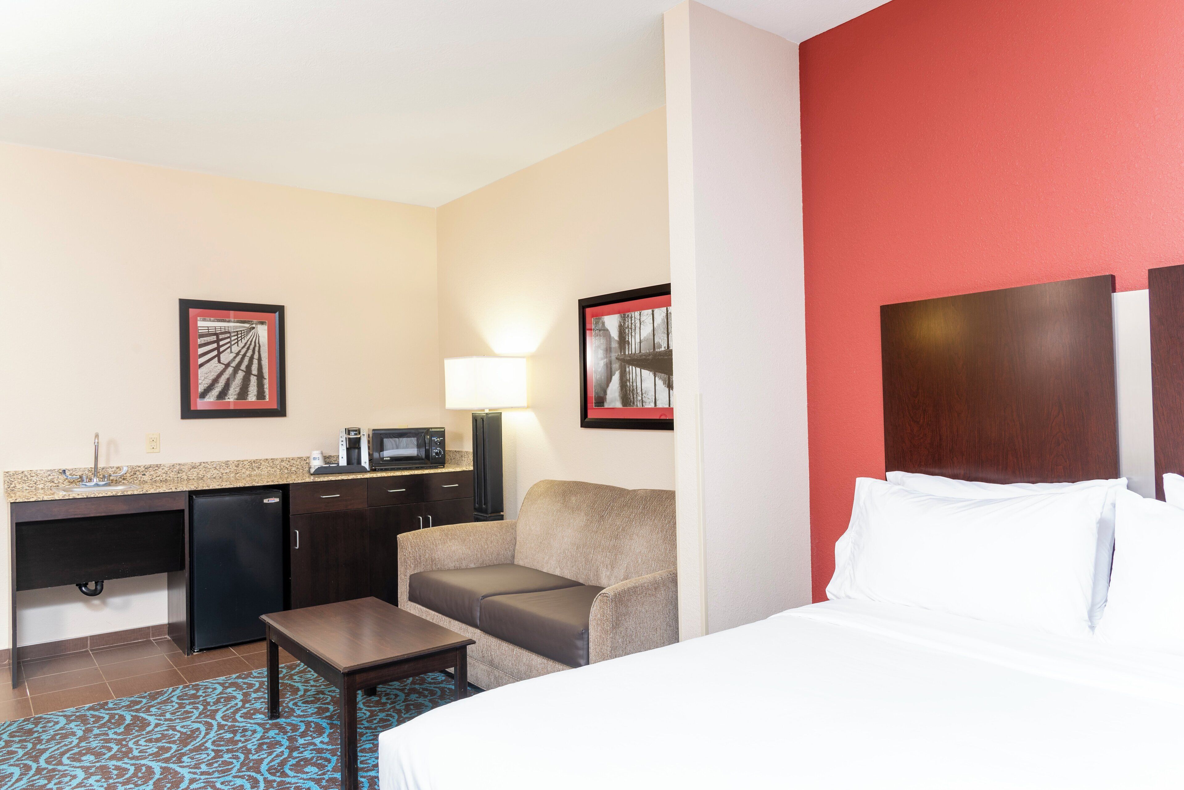 Une chambre d’hôtel équipée d’un lit, d’un bureau, d’une chaise, d’une machine à café et d’un four à micro-ondes.