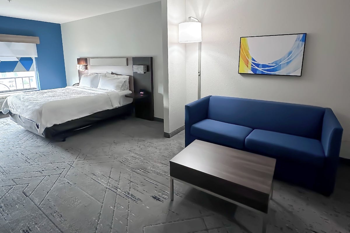 A hotel room with a bed, a blue sofa, a small table, and a painting on the wall.